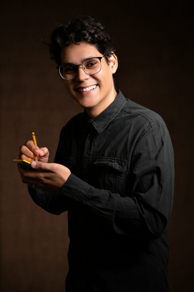 smiling man wearing black denim jacket holding pencil and sticky note while standing